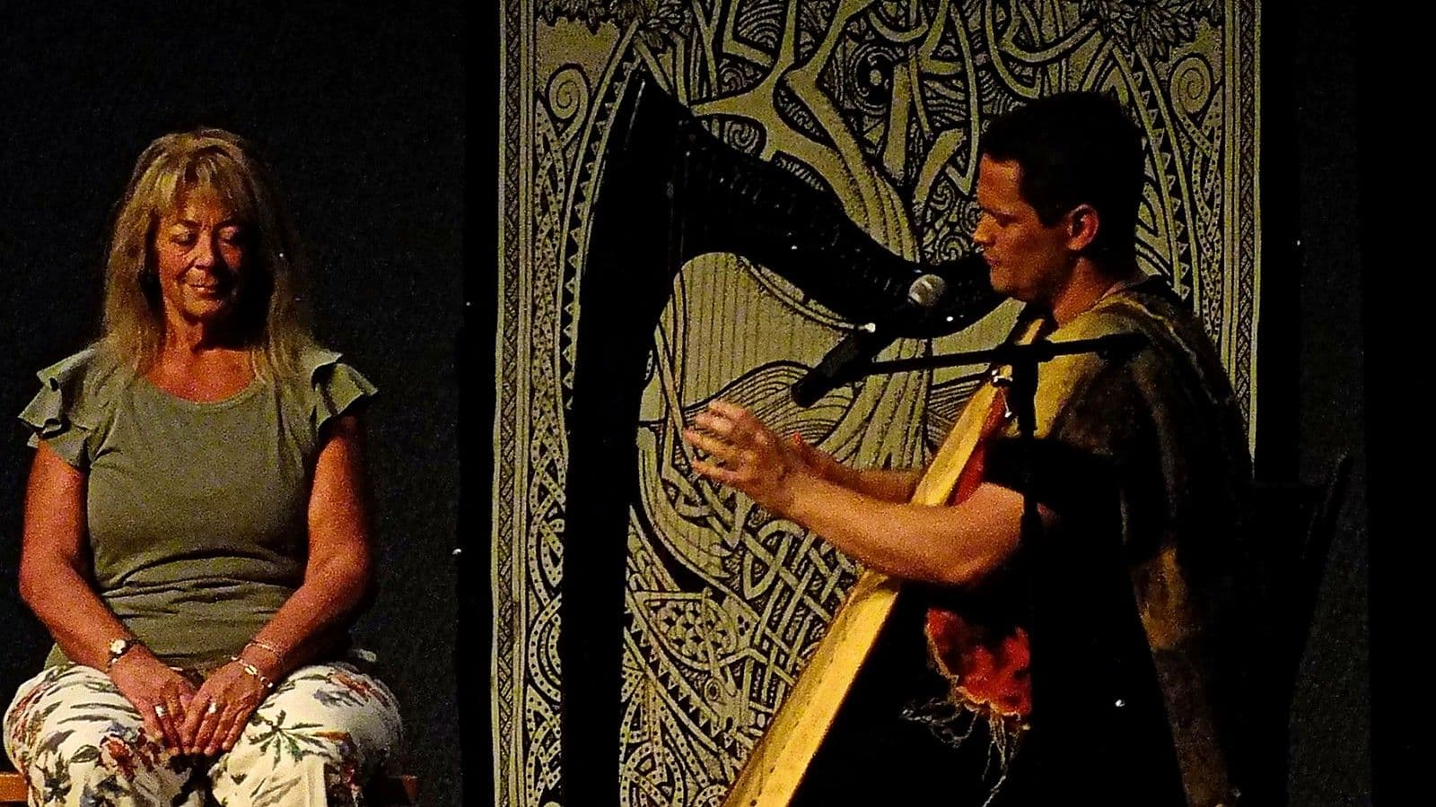 Russell playing the harp on stage while a woman listens with her eyes closed